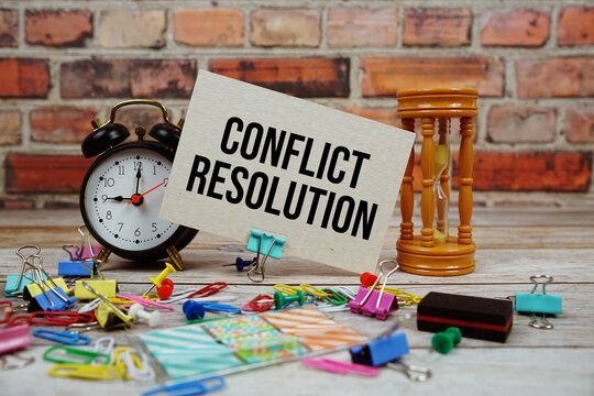 Conflict Resolution text on paper card with alarm clock and stationary on wooden background