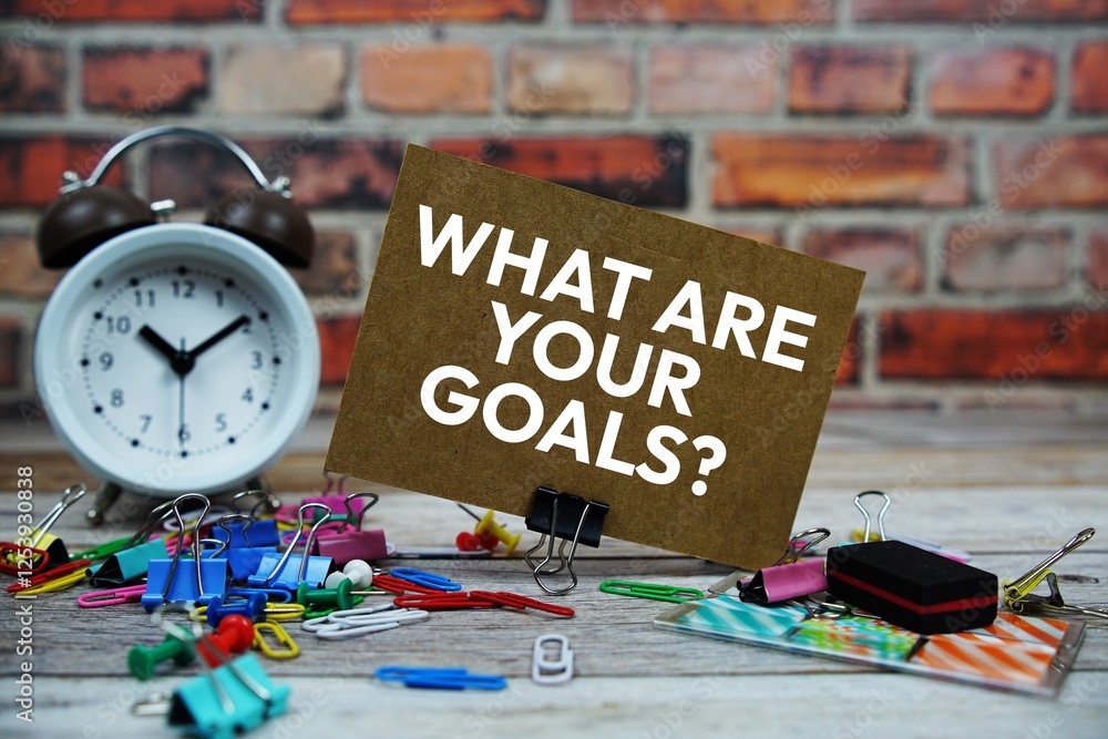 Poster what are your goals? text on paper card with alarm clock and stationary on wooden background