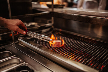 A close up shot of a delicious meat grilled in a restaurant kitchen with bright flames coming out of it