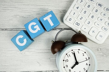 CGT (Capital Gain Tax) text with alarm clock and calculator on wooden background
