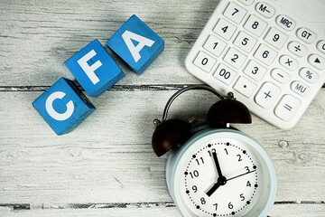 CFA (Chartered Financial Analyst) text with alarm clock and calculator on wooden background