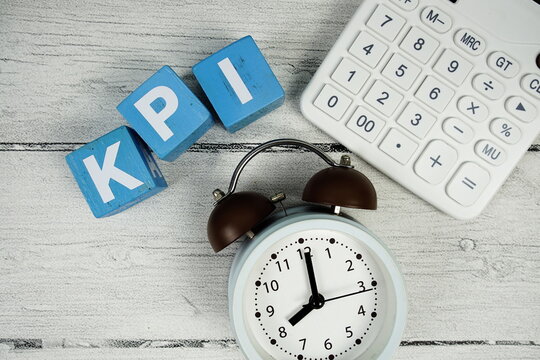 KPI (Key Performance Indicator text with alarm clock and calculator on wooden background - Powered by Adobe