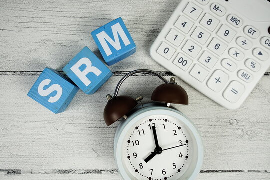 SRM (Sustainability Risk Management) text with alarm clock and calculator on wooden background