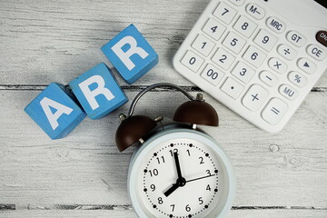 ARR (Annual Recurring Revenue) text with alarm clcok and calculator on wooden background
