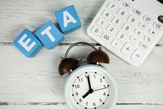 ETA (Estimated Time Of Arrival) text with alarm clock and calculator on wooden background