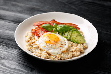 Savory Oatmeal breakfast with sunny side up fried egg, bacon and avocado. Healthy food