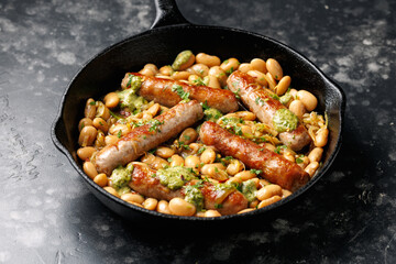 Creamy butter beans and sausages with kale pesto served in cast iron frying pan skillet