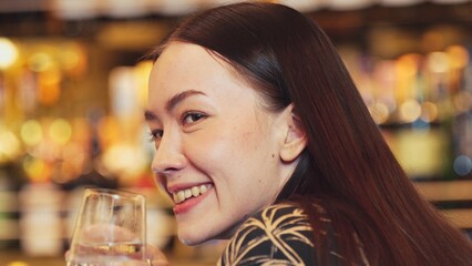Closeup woman guest drinking gin and tonic holding glass while talking with friend or couple at beverage bar counter scene. Beautiful face on blurred nightclub in bokeh lighting background. Vinosity.