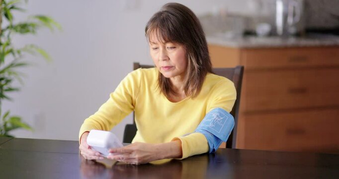 Woman sitting at home dining table alone talking own blood pressure reading using medical devise