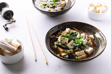Fresh traditional miso soup with tofu, shiitake mushrooms, green onion, wakame and spices on white background with copy space for your design. Traditional Japanese cuisine.
