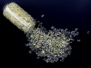 Natural colored polycarbonate plastic granules spilling from a glass tube, isolated on a black...