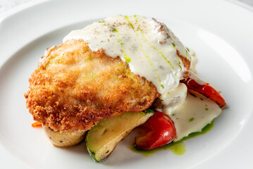 A deliciously plated dish featuring golden fried chicken topped with creamy sauce, served on a bed of sautéed vegetables including red peppers and zucchini. Perfect for a gourmet menu