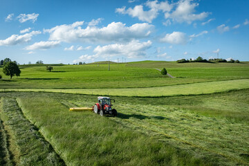 Grünfuttergewinnung im Allgäu - Traktor mit Mähwerk beim Gras mähen, Luftaufnahme.