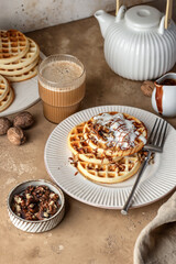 Belgian waffles with vanilla ice cream, nuts and chocolate topping for breakfast on beige textured table background