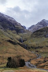 heart of glencoe in the scottish highlands, idyllic waterfall running down a majestic mountain painted in autumn colors, charming atmosphere of scotlands countryside