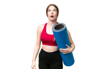 Young sport woman going to yoga classes while holding a mat over isolated chroma key background looking up and with surprised expression