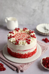 Red Velvet Cake with mascarpone and whipped cream on a plate, decorated with red currant. Pink napkin, grey background and white milk jug. 