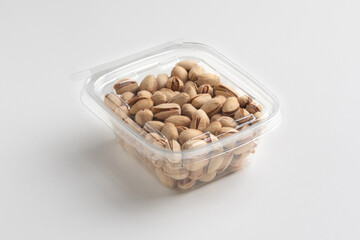 Nuts in a transparent plastic box isolated on white background, close up, food photography, mock up. Pile of toasted pistachios in plastic packaging.