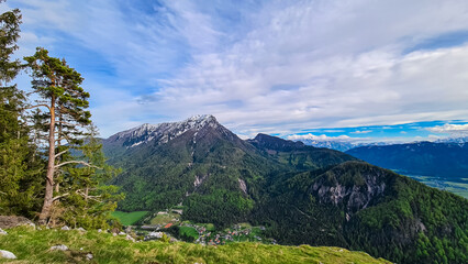 Iconic transmitter tower atop snow-capped Dobratsch mountain stands tall against clear blue sky. Jagged rocks and patches of evergreen forest cling to slopes, revealing rugged terrain of Gailtal Alps
