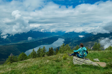 Hiker woman on grassy slopes near Mirnock with scenic view of Lake Millstatt in Carinthia, Austria. Alpine scenery with distant mountain peaks. Serene alpine landscape and green pasture, Austrian Alps