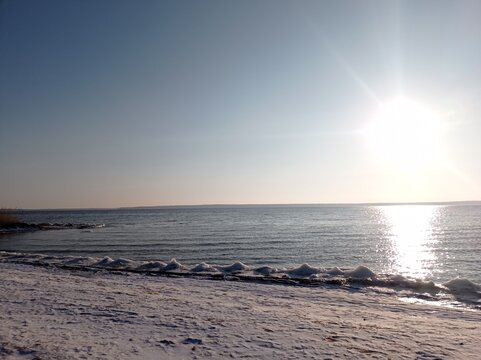 Serene Winter Seascape with Icy Shoreline and Calm Blue Waters, Capturing the Tranquility of a Frozen Beach at Sunset