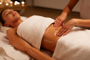 Professional masseur making relaxing massage of stomach for woman in calm spa center interior,...
