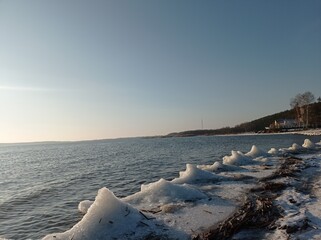 Serene Winter Seascape with Icy Shoreline and Calm Blue Waters, Capturing the Tranquility of a Frozen Beach at Sunset