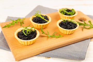 Tartlets with black caviar served on on wooden table