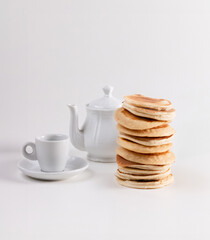  stack of pancakes sits on a white background, with a teapot and teacup in the background, creating a cozy, inviting breakfast scene.