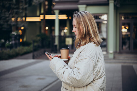 A young woman uses a smartphone and drinks coffee on the way to work.