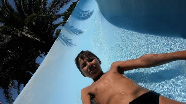 A boy slides down a blue water slide. High quality 4k footage