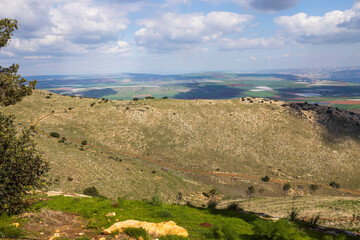 The view from Mount Gilboa overlooks pines, vegetation, the valley, and the Jordanian mountains, with clouds above and farmland below.