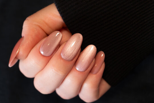 Oval-shaped extended nails with a glossy finish and "cat eye" effect look luxurious. The nude shade adds naturalness and softness. The hand visible wears a black sleeve.