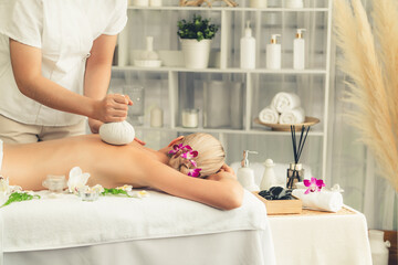 Hot herbal ball spa massage body treatment, masseur gently compresses herb bag on woman body....