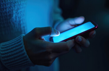 Hands hold smartphone in blue light in darkness. Finger touches device screen. Mobile phone glows. Social media, cyberspace communication. Modern digital tech contraption. Online browsing, texting.