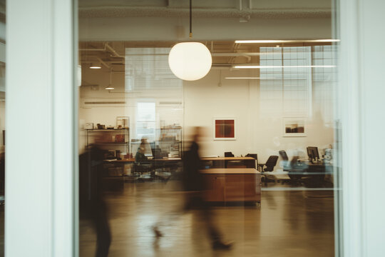 Blurred Motion in Office: A view through a glass door reveals a bustling modern office space, with employees moving in a blurred motion, hinting at a fast-paced and dynamic work environment.