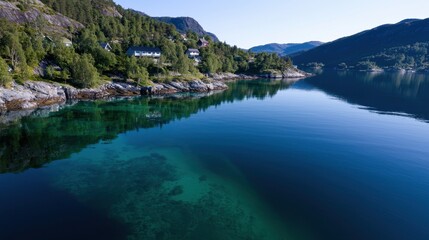 A stunning view of a calm fjord in Norway reveals crystal clear waters reflecting the surrounding hills and trees. Charming houses dot the shoreline, enhancing the tranquil atmosphere