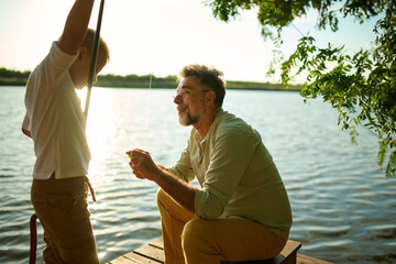 Grandfather helping grandson fixing fishing rod on pier