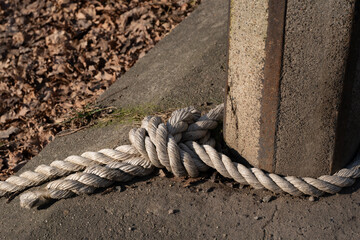 A thick, white rope tied in a strong knot around a weathered concrete post. The fibers of the rope appear slightly frayed, adding texture and character to the image. 