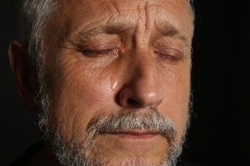 Sad senior man crying on black background, closeup