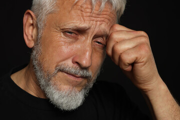 Sad senior man crying on black background, closeup