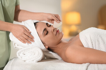 Young woman receiving facial massage with gua sha tool in spa salon