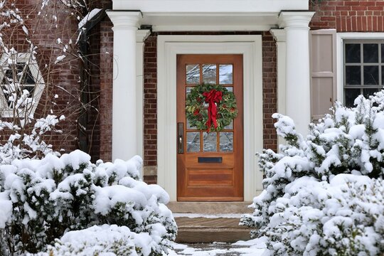 Traditional suburban home with shrubbery covered in snow and decorative wreath on front door