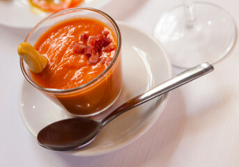 Glass bowl of cold salmorejo, pureed tomatoes and bread garnished with sliced ham