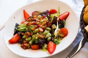 Colorful salad with candied beans, bacon marinated in soy-honey sauce, tomatoes, fruits and greens..