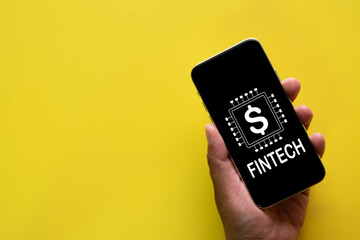  Photo of Fintech icon displayed on smartphone screen holding by hand on yellow background.,financial technology, mobile banking, digital payment, e-wallet, online transaction concept.