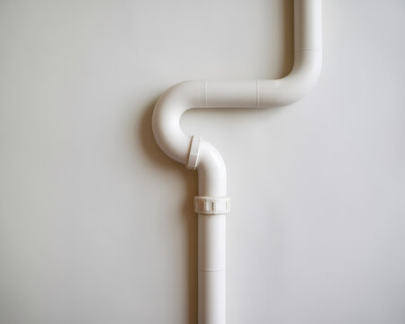 White pvc plumbing drain pipe with elbow joint and clamp on light wall background minimal home repair concept for bathroom sink water system installation maintenance construction and renovation