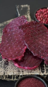Dried beef slices, jerky, with cherry or plum flavor, salt and spices on a dark concrete background