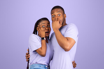 Obraz premium Omg. Portrait of scared African American couple covering mouth and eyes, woman jumping on man, looking at camera standing isolated on purple violet studio background. Human emotions, facial expression