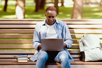 Excited black student looking at laptop screen, cannot believe his success at park. Young African American guy happy over passing difficult exam, receiving scholarship, getting excellent test grade